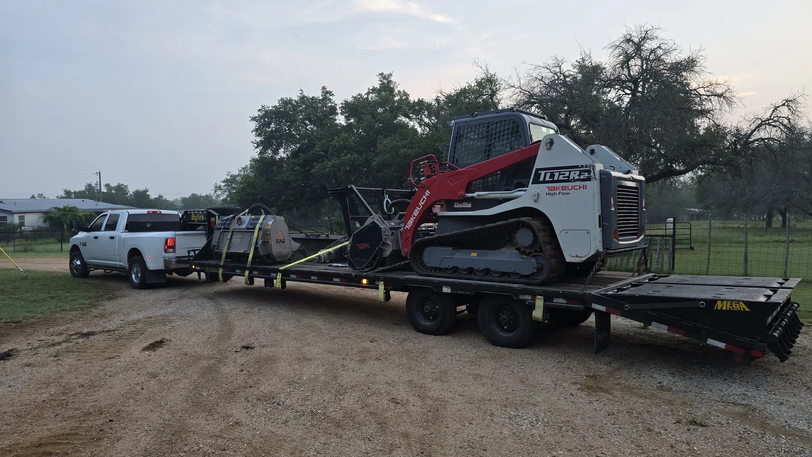 Pickup towing a trailer loaded with a tracked skid steer and mulching heads, land clearing equipment