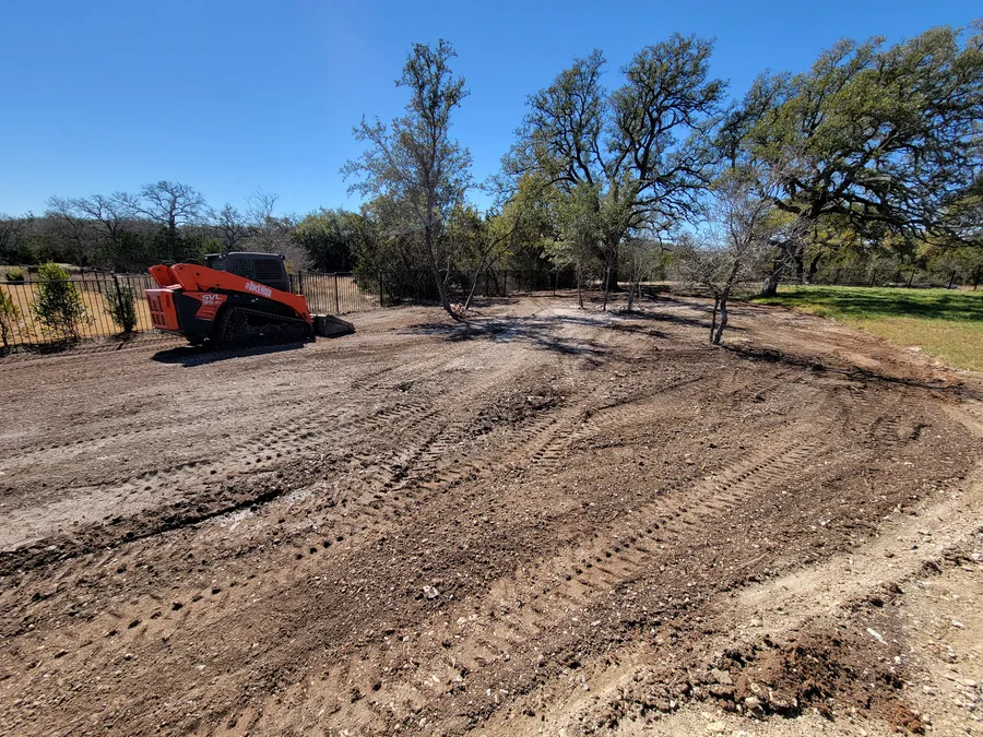 Tracked skid steer beside a freshly cleared and graded yard with the oaks kept, land clearing