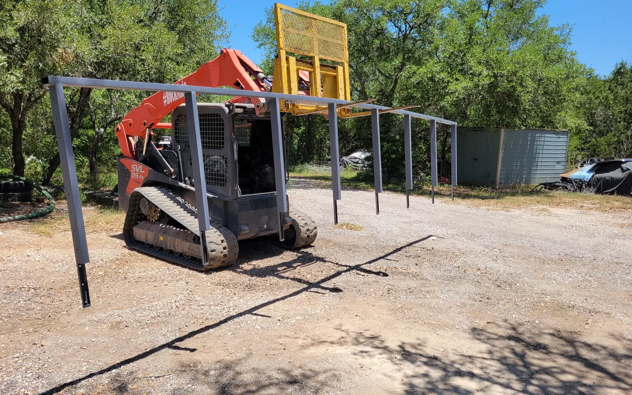 Tracked skid steer with pallet forks lifting a metal carport frame, light demolition