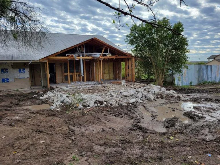 Old house partly torn down to the framing with broken concrete piled in front, light demolition