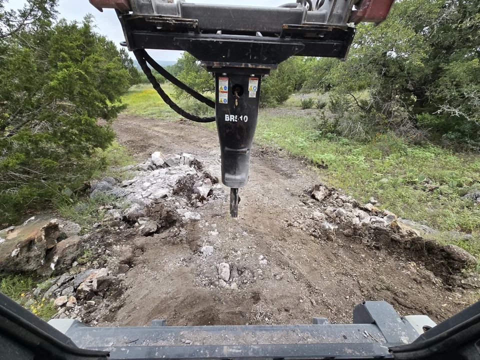 Hydraulic hammer on a skid steer breaking limestone rock on a trail, rock milling