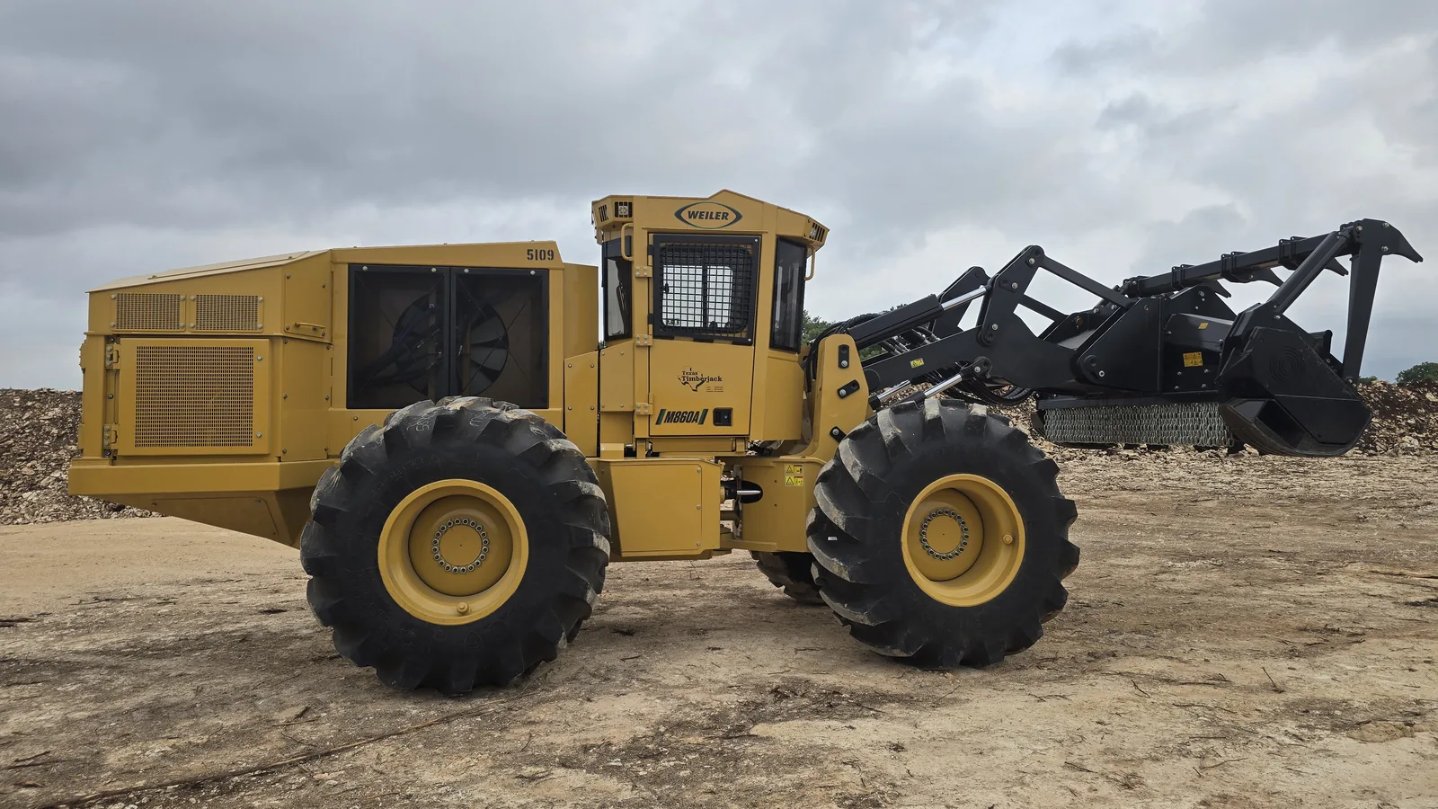 Wheeled forestry mulcher parked on a caliche work area with rock piles behind, land clearing