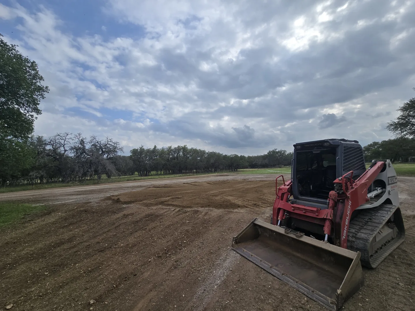 Tracked skid steer with a bucket on a freshly graded pad, site work