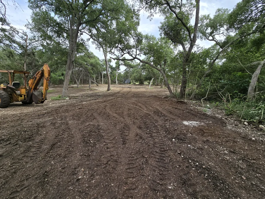 Backhoe beside a freshly graded road through oaks, site work